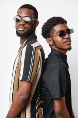 Siyah tenli, güneş gözlüklü ve arka arkaya poz veren Afro-Amerikalı erkekler. Son moda saç stilleri ve kendine güvenen ifadeleri olan iki genç erkeğin moda portresi..