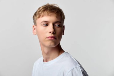 Beyaz tişörtlü düşünceli bir adam, basit bir stüdyo ortamında, sakin bir ifade, modern basitlik ve reklam, pazarlama ve hisse senedi projeleri için geniş uygulanabilirlik göstererek hafifçe geri dönüyor.