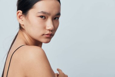 Yumuşak ciltli, koyu renk saçlı, düşünceli bakışlarla poz veren kadın modelin yakın çekimi. Temiz ten ve asgari giysi, doğal güzelliği, tarafsız arkaplanda hafif ışıklandırmayla ön plana çıkarıyor..