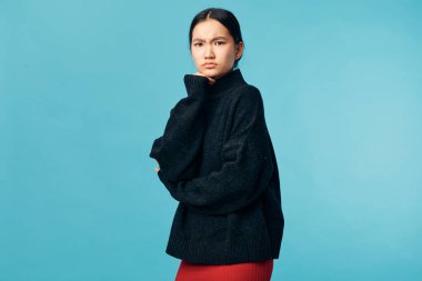 Siyah örgü süveter ve kırmızı etek giyen genç bir kadın. Çene üzerinde elle poz veriyor. Düşünceli bir görünüm ve sakin bir tavır takınıyor..