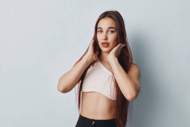 Stüdyoda sıradan kıyafetler giyen düz saçlı genç bir kadının portresi. Elleri yüze yakın poz veren kadın, doğal görünüm ve yaşam tarzı veya güzellik fotoğrafçılığı için stil gösteriyor..