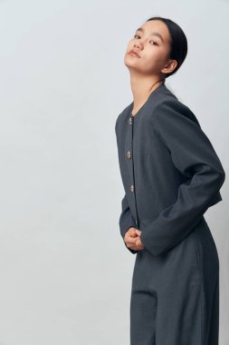 Kendine güvenen gri elbiseli genç bir kadının portresi. Manken, giysi ve minimalist görünüm için arka planda elleri arkada poz veriyor..