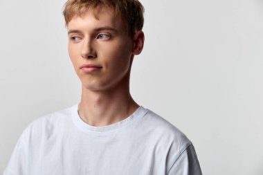 Beyaz tişörtlü kısa saçlı erkek figürü, profil görünümü, sakin ifade, basit arka plan, günlük moda ve günlük yaşam tarzı konsepti editoryal kullanım ve stok fotoğrafçılığı.