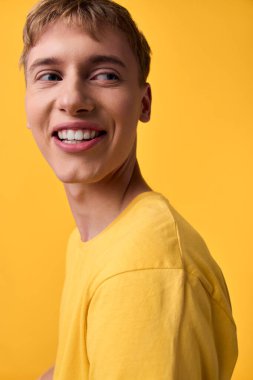 Sarı tişörtlü neşeli bir adam doğal ışıklandırma, gündelik poz ve iyimser ruh hali olan bir stüdyoda duruyor, modern, yaklaşılabilir bir ortamda marka, reklam ve yaşam tarzı kampanyaları için ideal.