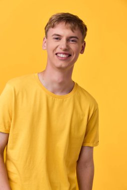Sarı gömlekli gülümseyen genç bir adamın günlük yaşam tarzı görüntüsü tek renkli sarı bir arka plana karşı, iyimser markalaşma, sağIık veya moda kullanımı için ideal..