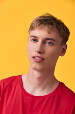 Kırmızı tişörtlü genç bir adamın yakın çekimi koyu sarı bir arka fonun yanında, gündelik moda, neşeli titreşim ve pazarlama görselleri için canlı kontrast vurguluyor..