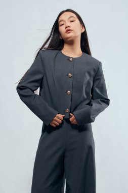 Dekoratif düğmeleri ve düz pantolonu olan gri takım elbiseli kendine güvenen bir kadının portresi. Minimalist stüdyo çekimi, temiz moda görüntüsü, iş için profesyonel ve şık kıyafetler..