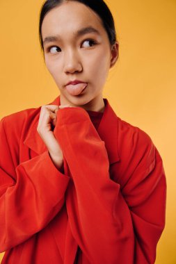 Kırmızı kıyafetli genç bir kadının portresi dil, renkli arkaplan, gayri resmi stil, stüdyo çekimi, doğal görünüş, eğlence havası ve duygusal yüz ifadesini gösteriyor..