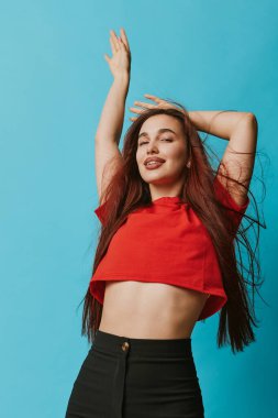 Kırmızı bluzlu, siyah pantolonlu, kolları havada, uzun saçlarıyla gülümseyen, sıradan moda portresiyle mavi arka planda dolaşan kendine güvenen bir kadın manken..