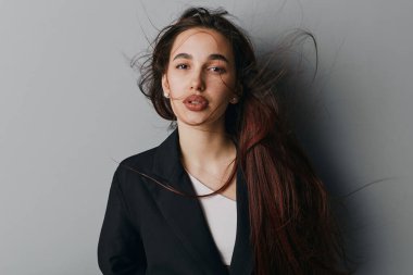 Siyah ceket ve beyaz bluz giyen dalgalı saçlı genç bir kadının portresi. Duvarın önünde duran doğal görünüşü ve moda fotoğrafçılığı için minimum makyajı olan bir kadın..