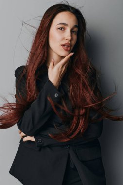 Gri duvarda duran kırmızı saçlı ve siyah ceketli genç bir kadının portresi. Çenesi ve ciddi ifadesi olan kadın model, hafif ışıklandırmalı profesyonel stüdyo resmi..