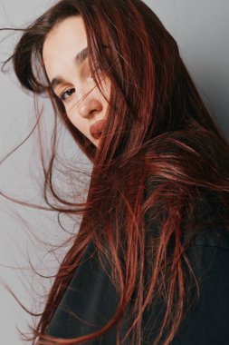 İçeride poz veren kızıl saçlı genç bir manken. Yakın plan portre, dağınık saçlar, doğal görünüş ve yumuşak ışıklandırma. Koyu renk tişörtlü, sakin bir yüz ifadesi ve az makyajlı bir kadın..