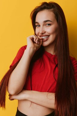 Sarı duvarın karşısında duran kırmızı saçlı, uzun düz saçlı, gülümseyen genç kadın. Kendine güveni tam bir kadın portresi ve yaşam tarzı ya da moda konsepti için rahat bir poz..