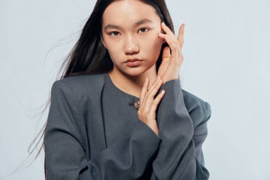 Düz saçlı ve gri elbiseli genç kadın modelin portresi. Moda, güzellik ve gelişigüzel fotoğraf çekimi için tarafsız gri arka planda el ele poz veriyor..