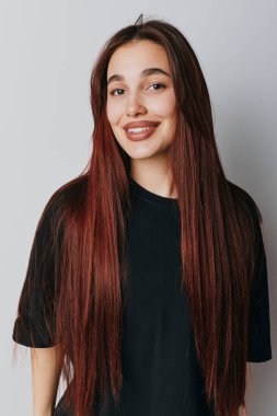 Uzun saçlı, siyah tişörtlü, gri duvarda duran gülümseyen kadın. Gençlik, gündelik moda, güzellik, özgüven ve doğal ifade..