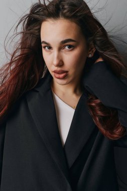 Siyah ceket ve beyaz gömlek giymiş dalgalı kahverengi saçlı genç bir kadın ciddi bir ifadeyle kameraya bakıyor. Saça dokunan kadın modelin stüdyo görüntüleri..