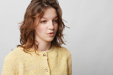 Tarafsız bir arkaplanda sarı kazak giymiş kıvırcık kahverengi saçlı düşünceli genç bir kadının portresi. Stüdyoda içgözlem, günlük moda ve doğal ifade kavramı.