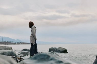 Gündelik giysiler içinde yalnız bir kadın deniz kenarındaki taşların üzerinde duruyor bulutlu bir gökyüzünün altındaki ufka bakıyor. Huzurlu kıyı manzarası sakinliği, iç güzelliği ve doğal güzelliği çağrıştırıyor..