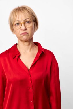 Kırmızı gömlek ve gözlük takan mutsuz orta yaşlı kadın rahatsız ve şüpheci görünüyor. Beyaz arka planda izole edilmiş, tatminsizlik, hayal kırıklığı ve olumsuz duygular konsepti..