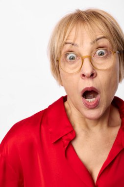 Kırmızı gömlekli, ağzı açık ve beyaz arka planda geniş gözleri olan şok olmuş olgun bir kadının yakın çekimi. Şaşkınlık, şaşkınlık ve anlamlı duygu kavramı..