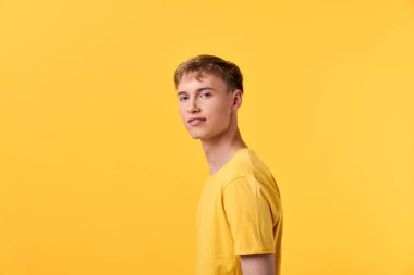 Sarı tişörtlü sıradan bir erkek model güçlü sarı bir arka plana karşı poz veriyor, parlak bir stüdyo çekimi moda, gençlik tarzı ve marka tasviri için ideal..