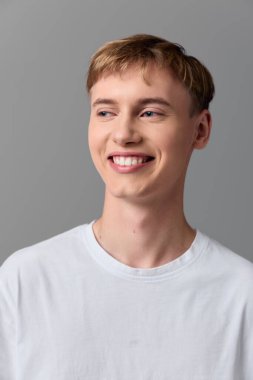 Basit bir stüdyo ortamında beyaz tişört giyen neşeli bir erkek. Yumuşak doğal ışık, nötr zemin ve gevşek duruş pazarlama, web veya internet için modern yaşam tarzı görüntülerini iletir.