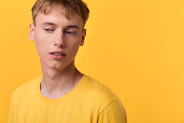Sarı tişört giyen erkek model, sıcak sarı bir arkaplan önünde poz veriyor, rahat duruş ve odaklanmış bakışlarla canlı, çağdaş bir ruh hali sunuyor, moda ve yaşam tarzı projeleri için ideal..