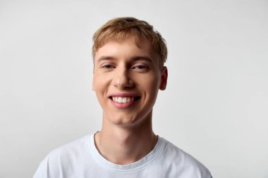 Rahat bir ortamda beyaz t-shirt giyen mutlu genç adam, hafif ışıklandırma, yaklaşılabilir titreşim, basit bir arka plan, pazarlama, reklam ve portföy kullanımı için idealdir.