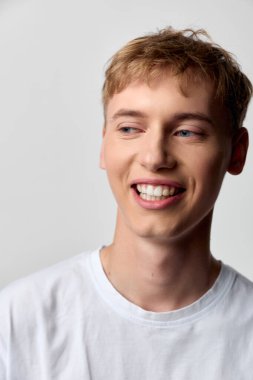 Basit bir beyaz tişört giyen, reklam kampanyaları, sosyal medya ve günlük yaşam tarzı ürünleri için uygun güven ve rahatlık sergileyen gülümseyen genç bir adamdan parlak ve neşeli bir titreşim..