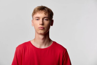Stüdyoda sade bir arkaplan önünde kırmızı tişörtlü gençlik, sakin görünüm ve ileri bakış, temiz estetik ile pazarlama, reklam ve tasarım projeleri için ideal