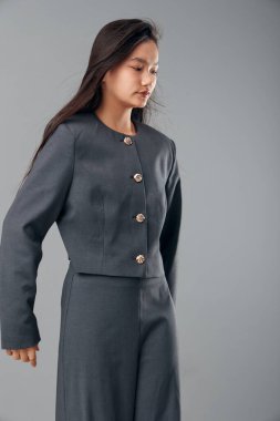 Koyu gri, yüksek belli etek giyen ve düğmeleri tarafsız arkaplanda duran uyumlu ceket giyen bir kadın manken. Kurumsal görünüş, iş kadını, resmi kıyafet ve modern kıyafet tarzı..