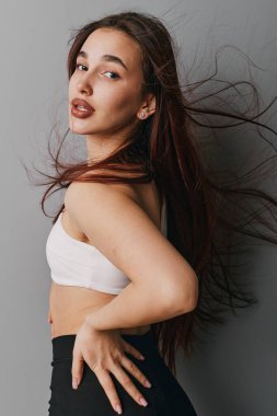 Şık, genç bir kadının portresi dalgalı saçlar ve el ele poz veren günlük kıyafetler. Pürüzsüz ciltli ve minimalist stüdyo ortamında rahat durabilen bir kadın model..