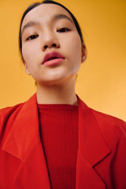 Doğal makyajlı, kırmızı elbiseli, sarı arka planlı kadın modelin yakın çekimi. İfade sakin ve kendinden emin, çağdaş moda ve minimalizmi kapalı mekanda vurguluyor..