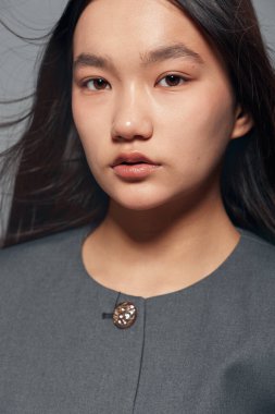 Makyajsız poz veren ve gri kıyafetli genç bir kadın. Yüz hatlarını ve doğal güzelliklerini gösteren, pürüzsüz ciltli ve basit desenli giysileri olan bir kadın..