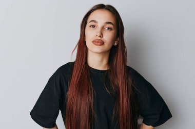 Confident young woman with long hair posing with hands on hips in black t shirt. Casual portrait with natural look and relaxed expression on neutral background in studio setting.