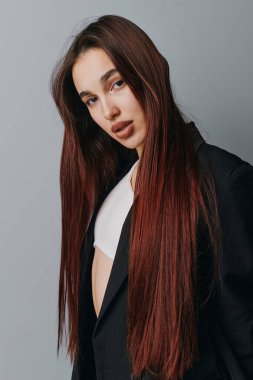 Portrait of young female model with long brown hair in black jacket and white shirt. Studio shot with neutral backdrop, casual pose, and natural look for fashion and lifestyle concept.