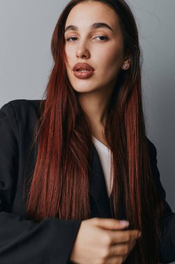 Uzun kırmızı saçlı, siyah ceketli, beyaz gömlekli, objektif yüzlü ve rahat duruşu olan kameraya bakan kendine güvenen genç bir kadının portresi..