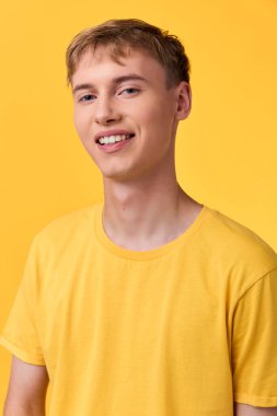 Sarı tişört giyen neşeli genç adam tek renkli sarı bir ortamda pozlar veriyor, parlaklığı, iyimserliği ve günlük yaşam tarzını ticari, yaşam tarzı veya marka kullanımı için uygun gösteriyor..