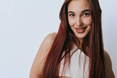 Stüdyoda poz veren kızıl saçlı, gülümseyen genç bir kadın. Mutlu ifadeli kadın portresi, doğal görünüş, ve sade ışık arkaplanı üzerinde rahat duruş.