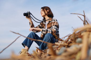 Kadın fotoğrafçı dışarıda, uzun kamışların arasında bir kamera tutuyor, atmosfer ışığını kovalıyor özenle, ifadeyle ve maceracı ruhla bir manzara karesi hazırlıyor..