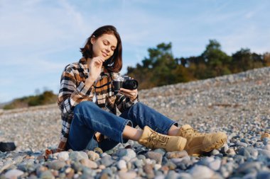 Taşların arasında fotoğraf makinesi olan bir kadının sıradan dış portresi. Yaratıcı anı ve manzarayı yakalıyor. Saçlarında güneş ışığı rüzgarı ve rahatlamış odaklanmış bir ruh hali var.