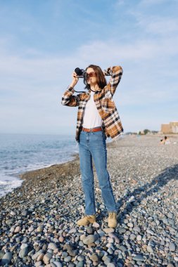 Kayalık sahilde kameralı, ekose gömlekli, kot pantolonlu ve güneş gözlüklü, okyanus ufkunu çerçeveleyen, deniz kenarında gündüz fotoğrafçılığının keyfini çıkaran, huzurlu ve maceracı bir hayat tarzı portresi olan sıradan bir gezgin..