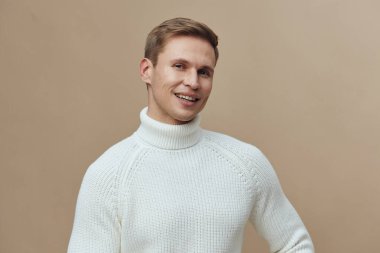 smiling caucasian man wearing white turtleneck sweater look camera in studio portrait with beige background represent digital nomad remote work and freelance concept with casual lifestyle happy young
