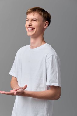 Basit beyaz tişörtlü neşeli adam açık jest yapıyor, gevşemiş ve cezbedici ruh hali pazarlama, sosyal medya veya öğretici içerik için ideal sıcaklığı ve ulaşılabilir iletişimi vurguluyor.