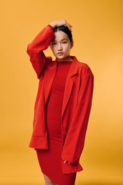 Sarı arka planda duran kırmızı elbiseli kadın model, zarif ve şık görünümlü kısa saçlı, minimalist moda konsepti, göz teması olan stüdyo çekimi.