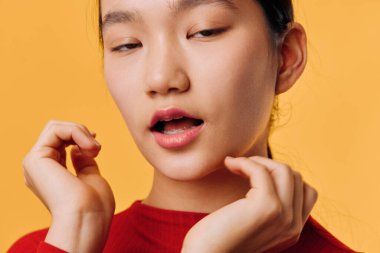 Female model in red shirt with relaxed face and slightly open mouth posing with hands close to head on bright orange backdrop. Beauty, emotion and closeup portrait with soft natural light.