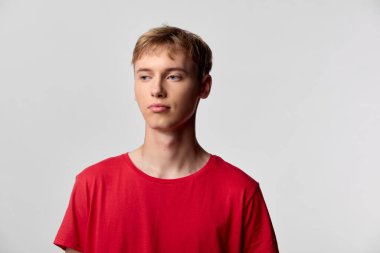 Kırmızı gömlekli genç adam sade bir arkaplan önünde poz veriyor, basit bir modern görünüm sunuyor, reklam, editör ve pazarlama görselleri için çok yönlü bir cazibesi var.
