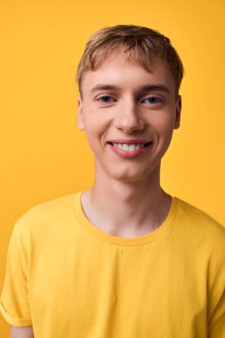 Sarı tişörtlü sıradan bir genç, canlı bir arka planda duruyor, mutluluk saçıyor ve yaşam tarzı, moda ve yaratıcı stok kullanımı için uygun yaklaşılabilir enerji yayıyor.