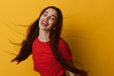 Sarı arka planda kırmızı tepeli, uzun siyah saçlı, gülen ve gülümseyen genç bir kadın. Pozitif duygu, doğal görünüş ve kaygısız ruh hali canlı renkli bir ortamda yakalanır..