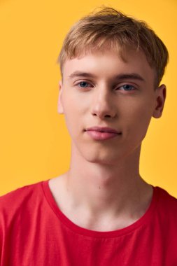 Kırmızı tişört giyen, sarı arka plan, stüdyo ışıklandırması özellikleri ve pazarlama, markalaşma ve kurumsal görseller için uygun dostane, yaklaşılabilir bir ruh hali içinde genç bir adama yakın durun.